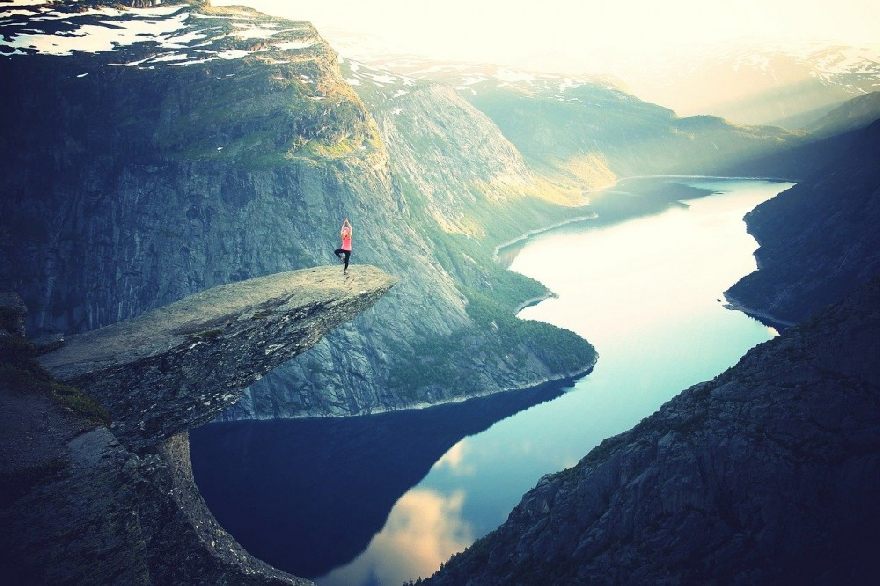 Gebeamter Mensch auf einer Klippe auf einem Berg, der Yoga macht.